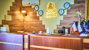 A hotel reception desk with a wooden design, clocks displaying different city names, and flags representing various countries. - Leotel Hotel (Lviv)