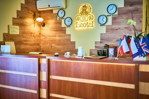 Un mostrador de recepción de hotel con diseño de madera, relojes mostrando nombres de diferentes ciudades e insignias que representan a varios países.