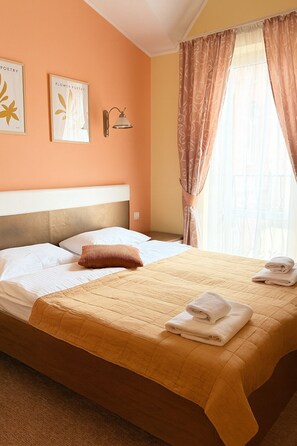 Une chambre d’hôtel avec un lit, des oreillers, une tête de lit, une lampe fixée au mur et des rideaux.