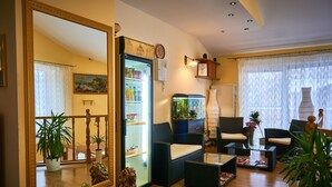 A living room with a large mirror, a refrigerator stocked with beverages, wicker furniture, and several potted plants. - Leotel Hotel (Lviv)