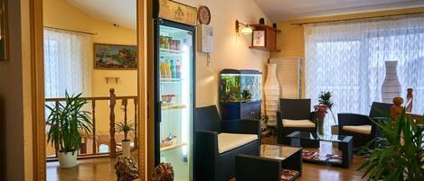 Uma sala de estar com um espelho grande, uma geladeira repleta de bebidas, móveis de vime e várias plantas em vasos.
