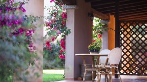 An outdoor patio with a table and chairs, surrounded by lush greenery and flowering plants. - S'Incantu Resort (Villasimius)