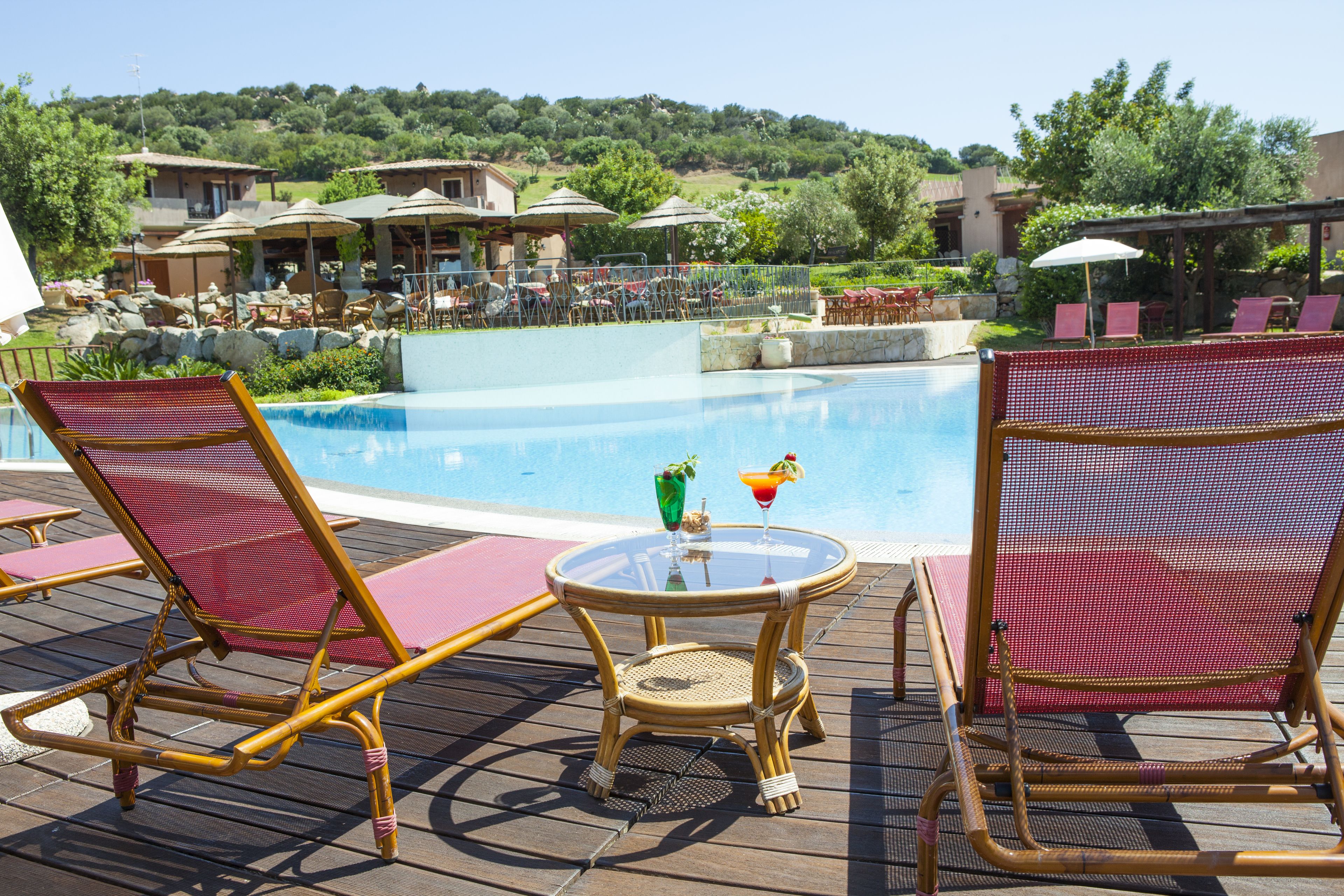 Zona de piscina amb gandules i ombrelles, una taula petita amb begudes i vista del paisatge circumdant.