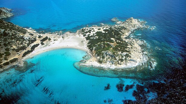 An aerial view of a coastal area with a sandy beach, clear blue waters, and rocky outcrops. - S'Incantu Resort (Villasimius)