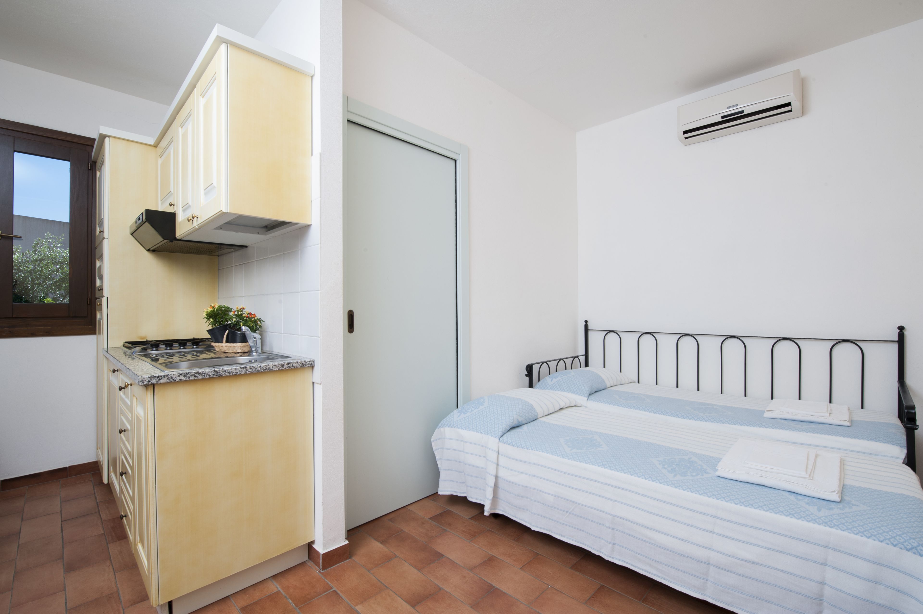 A compact room with a kitchenette, a bed, and a window.