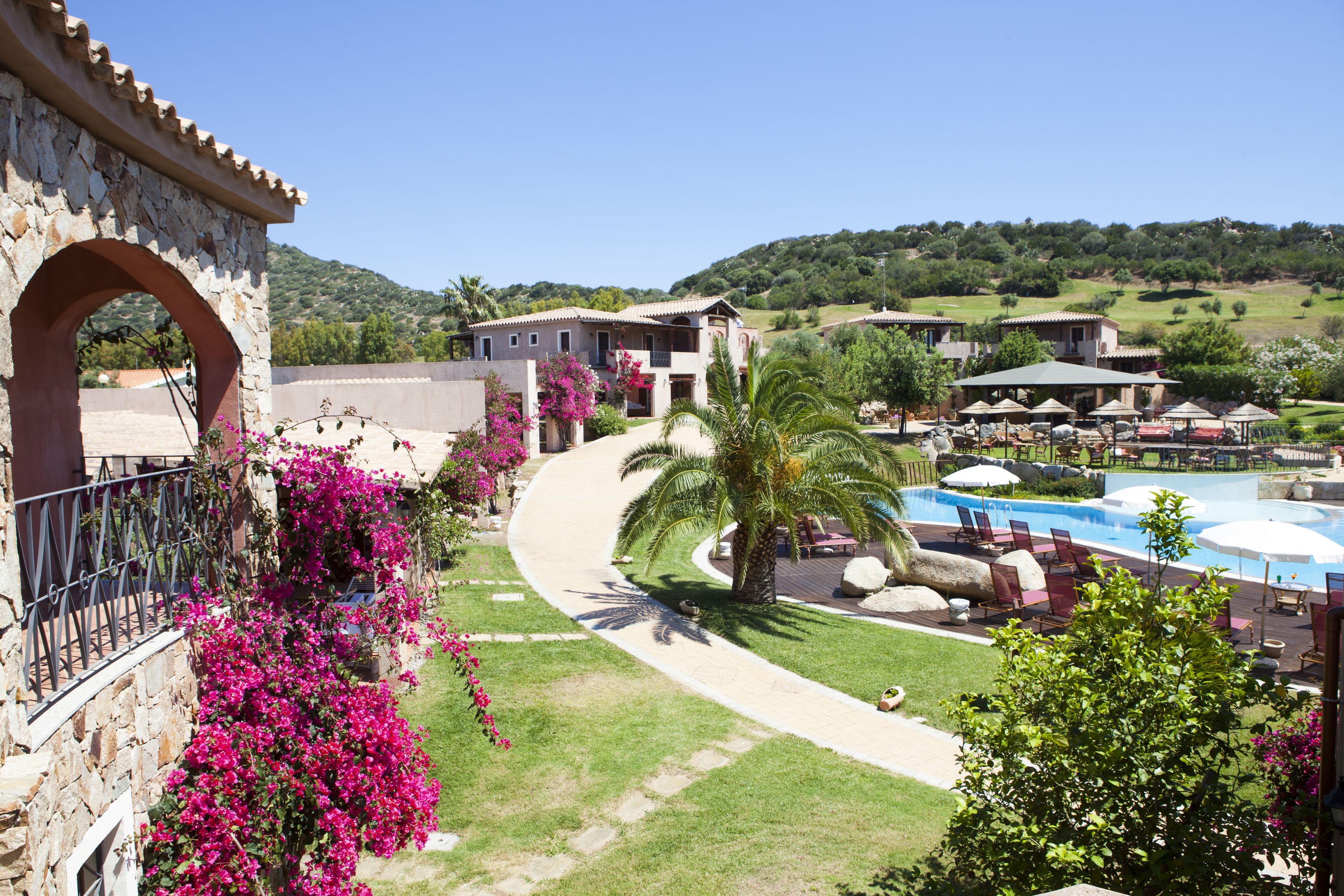 Un resort con piscina, palme e un edificio in pietra con un arco.