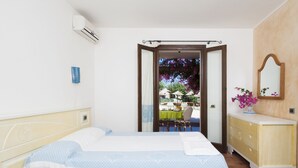 A bedroom with two beds, a dresser, and a view of an outdoor dining area. - S'Incantu Resort (Villasimius)