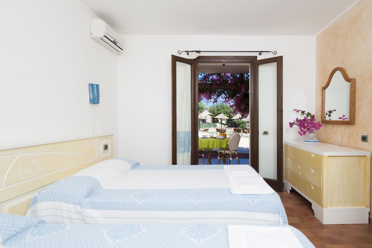 A bedroom with two beds, a dresser, and a view of an outdoor dining area.