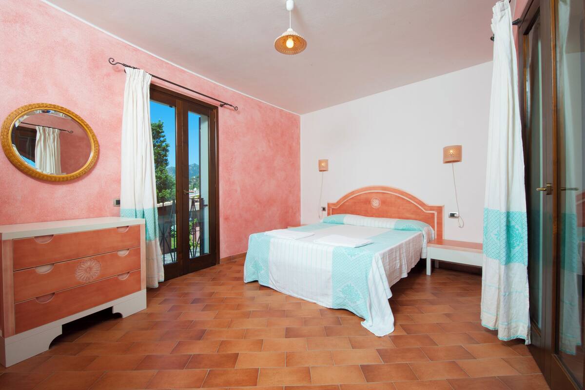 A bedroom with a bed, a dresser, a mirror, and a window with curtains.