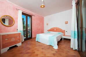A bedroom with a bed, a dresser, a mirror, and a window with curtains. - S'Incantu Resort (Villasimius)