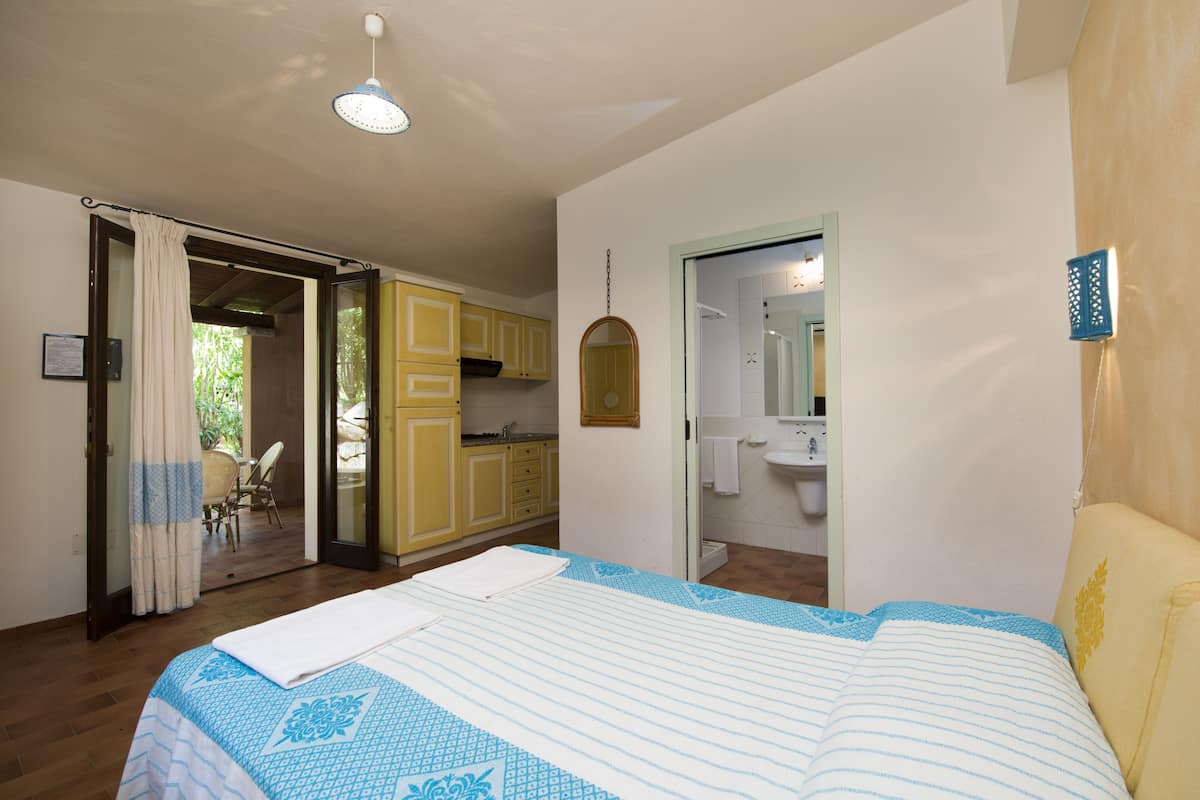A bedroom with a bed, a bathroom with a sink, and a kitchen area.