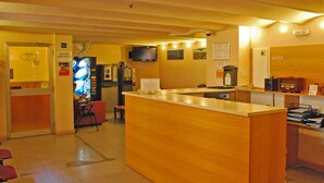 Zona de recepción con mostrador de madera, televisor montado en la pared y señalización de acceso a WiFi.