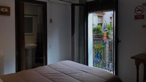 Habitación de hotel con cama, aire acondicionado, baño y balcón con vistas a la calle y edificios.