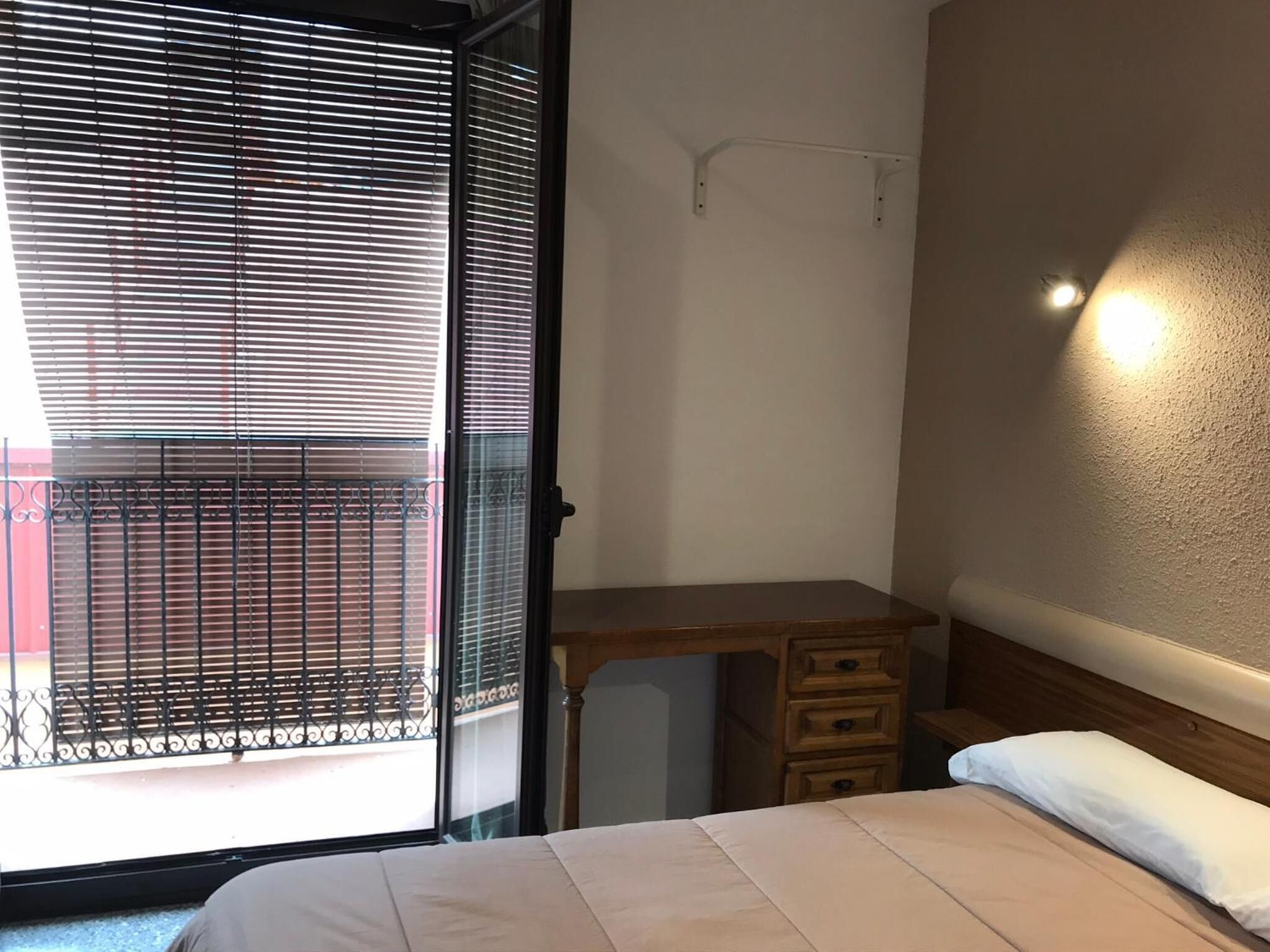 Ein Schlafzimmer mit einem Bett, einem Holztisch und einem Fenster mit Jalousien.