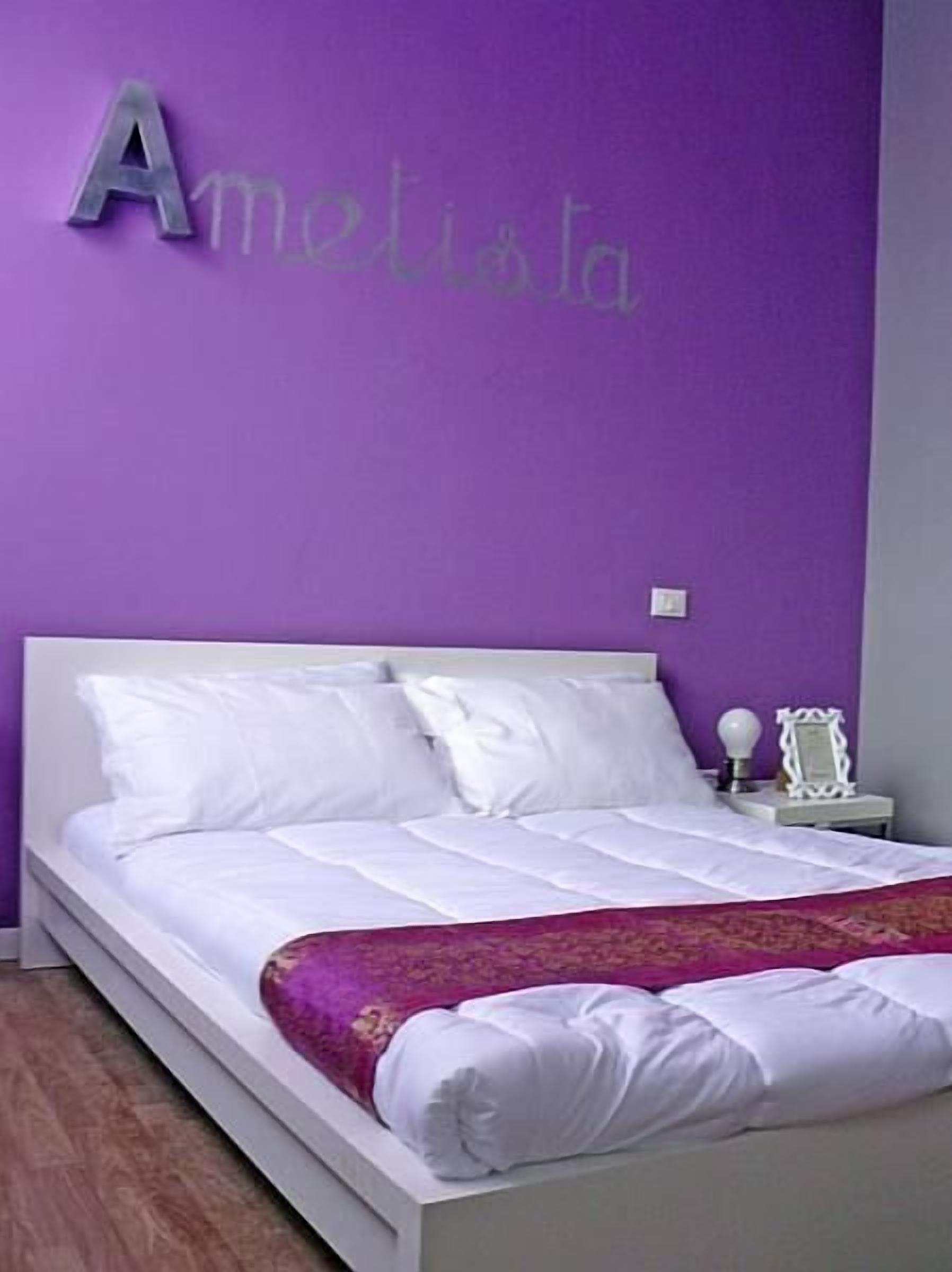 Una cama con sábanas blancas y una pared morada con la palabra "Amelita" en la parte superior.