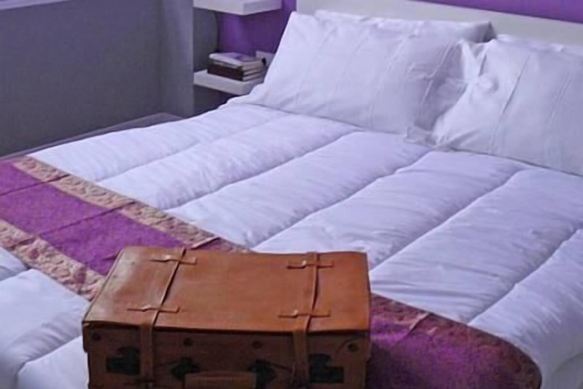 A bedroom with a purple wall, a white bed, and a small wooden chest on the bed.