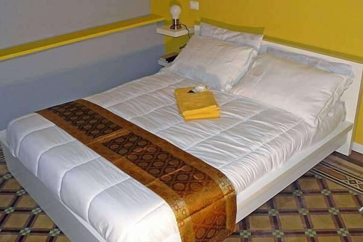 A bed with white linens, a patterned throw, and a yellow towel.