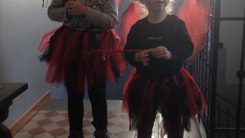 Two children in red and black costumes with wings, standing in a room with a checkered floor and a window with blinds.