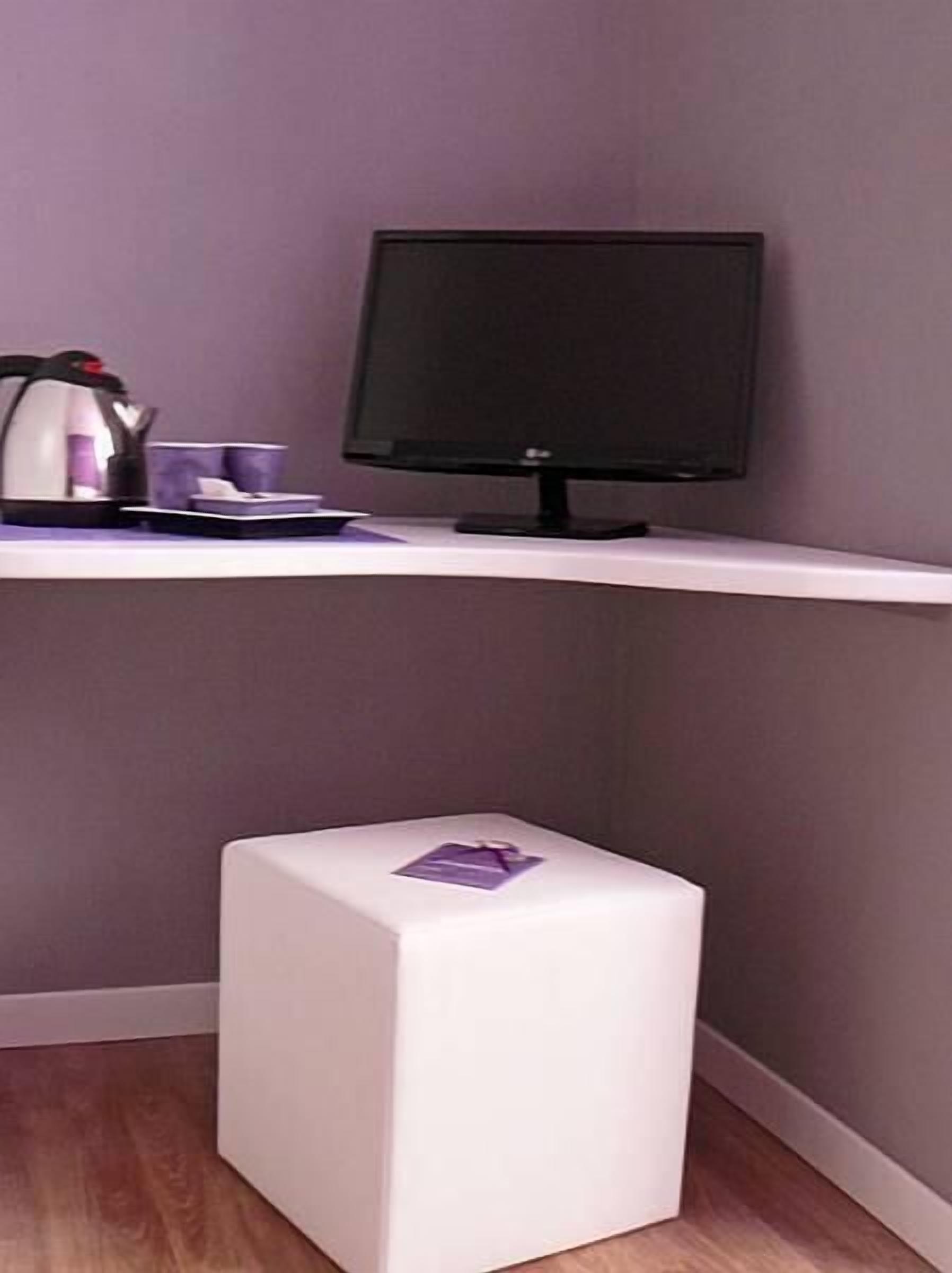 Un escritorio pequeño y blanco, de forma cuadrada, con un monitor negro, una tetera y una taza encima.