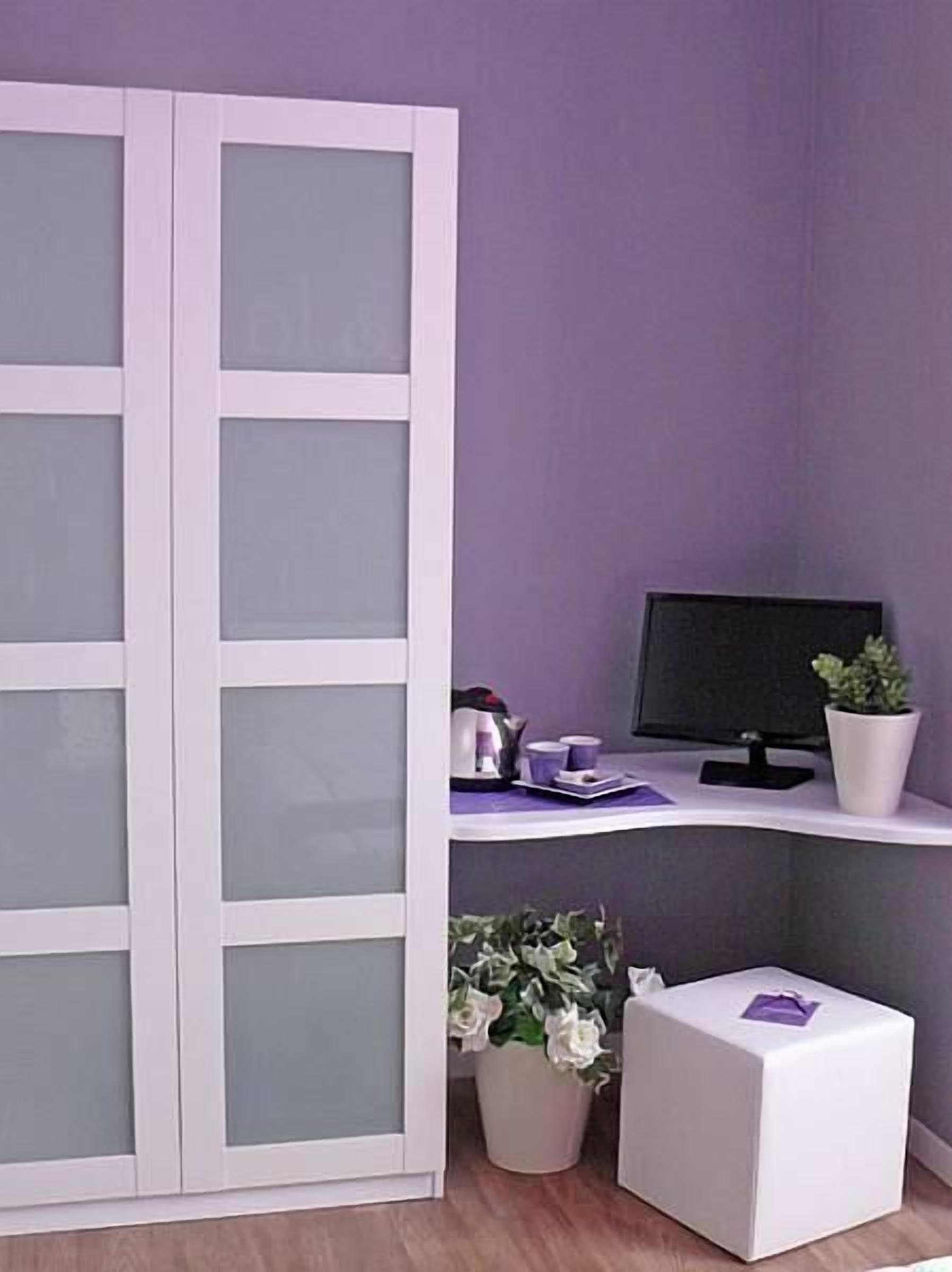 Een kamer met een witte kast met geëtste glazen panelen, een bureau met een computer monitor, een potplant en een zakdoekendoos.