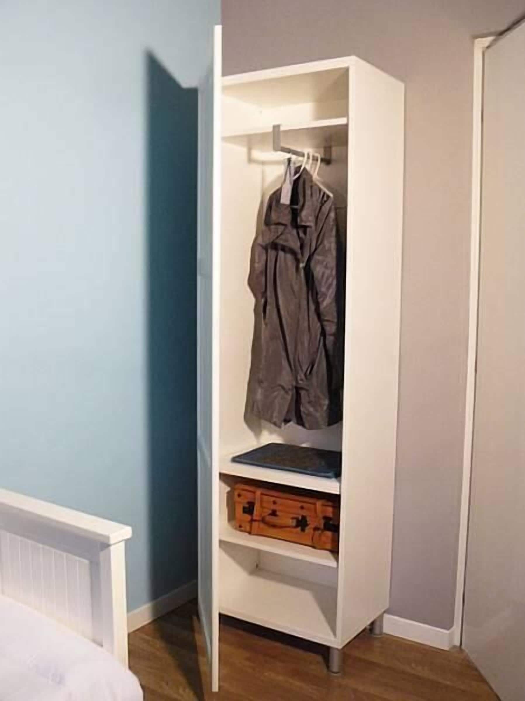 Ein weißer Kleiderschrank mit Kleiderstange und einem darunterliegenden Fach für einen Koffer.