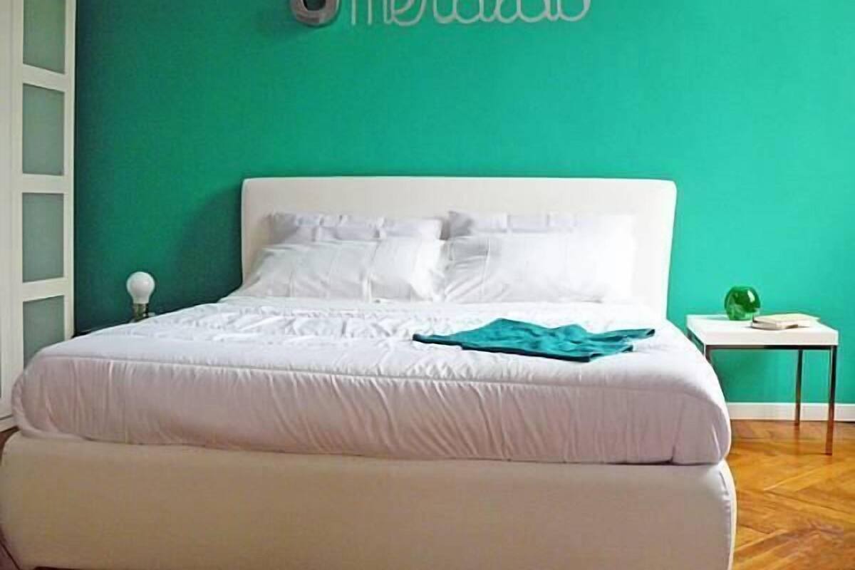 A bedroom with a white bed, teal walls, and a sign that reads "Smeraldo".