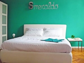Ein Schlafzimmer mit einem weißen Bett, tealfarbenen Wänden und einem Schild mit der Aufschrift 'Smeraldo'.