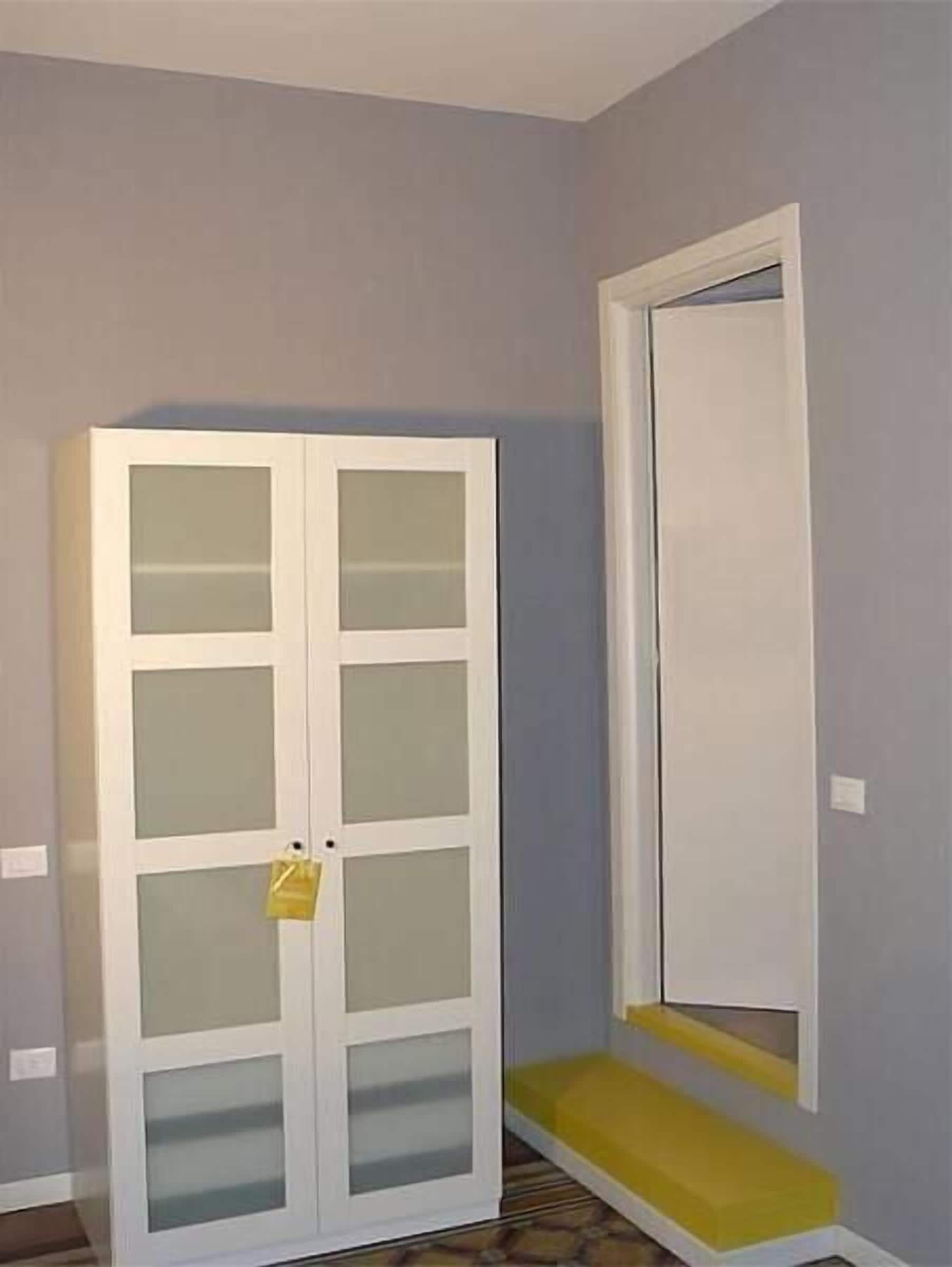 Une pièce avec une armoire blanche, un banc et une porte.
