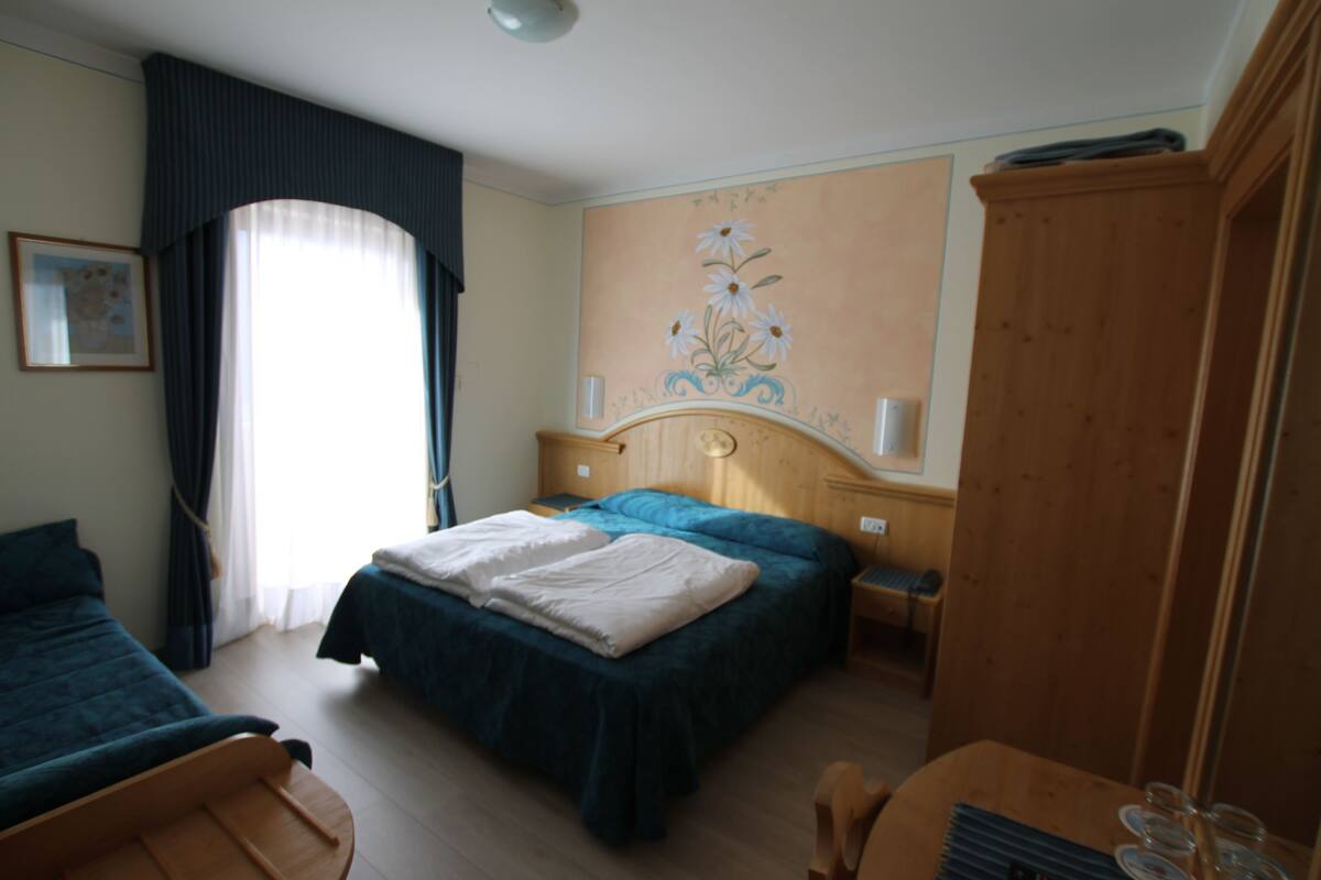 A hotel room with two beds, a wooden wardrobe, a desk with a chair, and a painting on the wall.