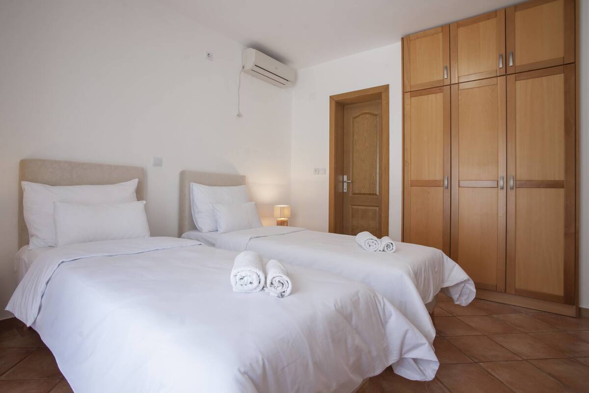A hotel room with two beds, a wardrobe, and an air conditioning unit.