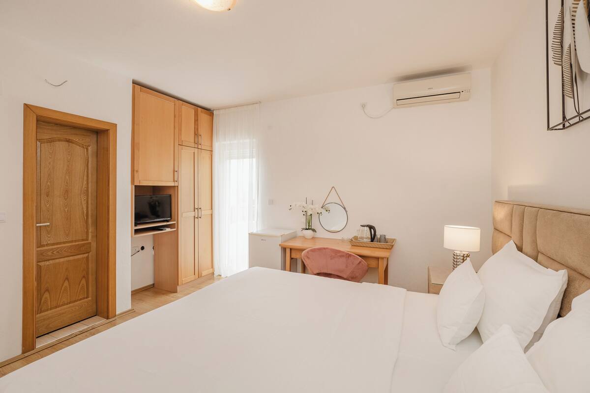 A bedroom with a bed, a desk, a chair, a TV, and an air conditioning unit.