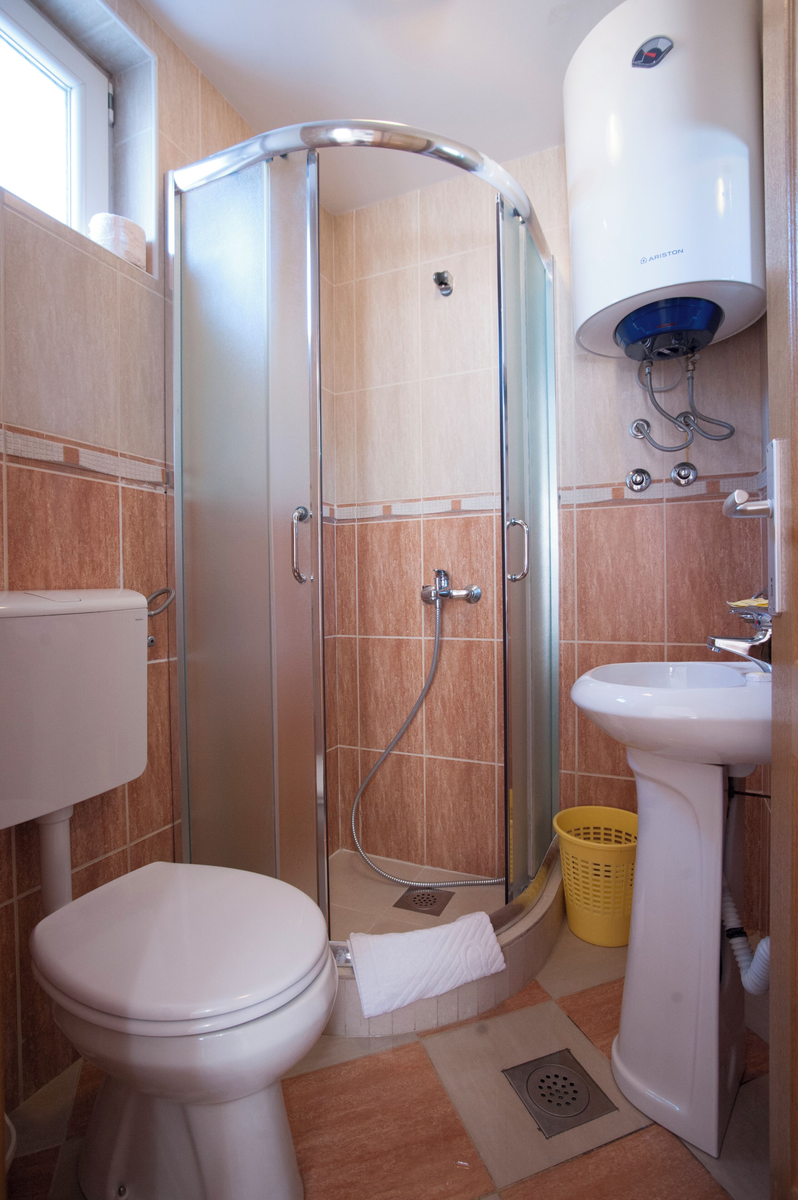 A bathroom with a glass-enclosed shower, a toilet, a sink, and a white heater.