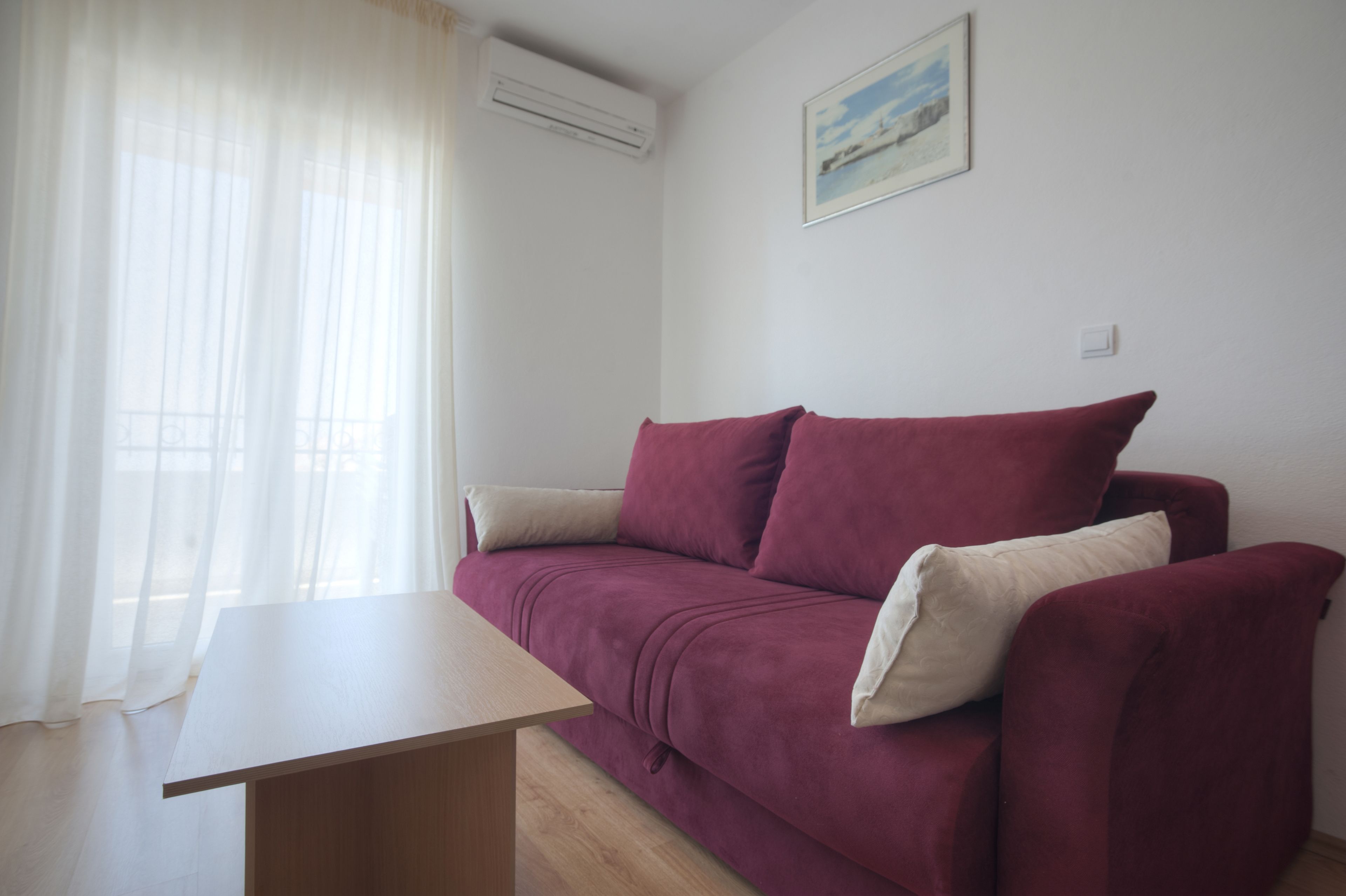 A room with a wooden table, a red sofa, and a white air conditioning unit on the wall.