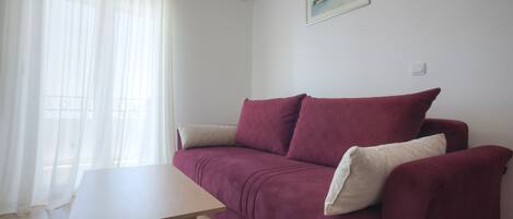 A room with a wooden table, a red sofa, and a white air conditioning unit on the wall.