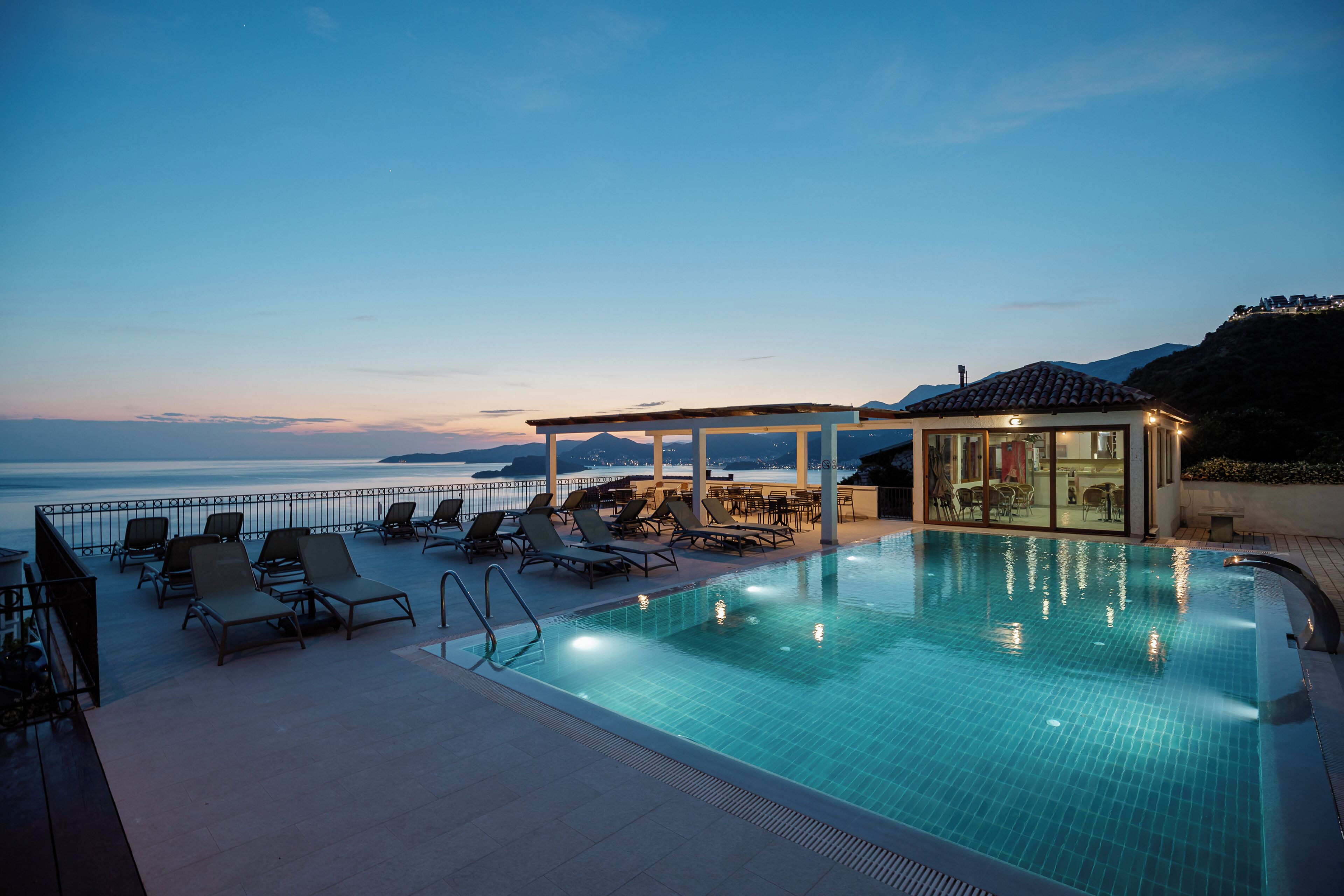 A swimming pool with lounge chairs and a glass-enclosed area, overlooking a body of water.