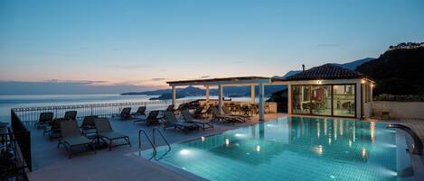 A swimming pool with lounge chairs and a glass-enclosed area, overlooking a body of water.