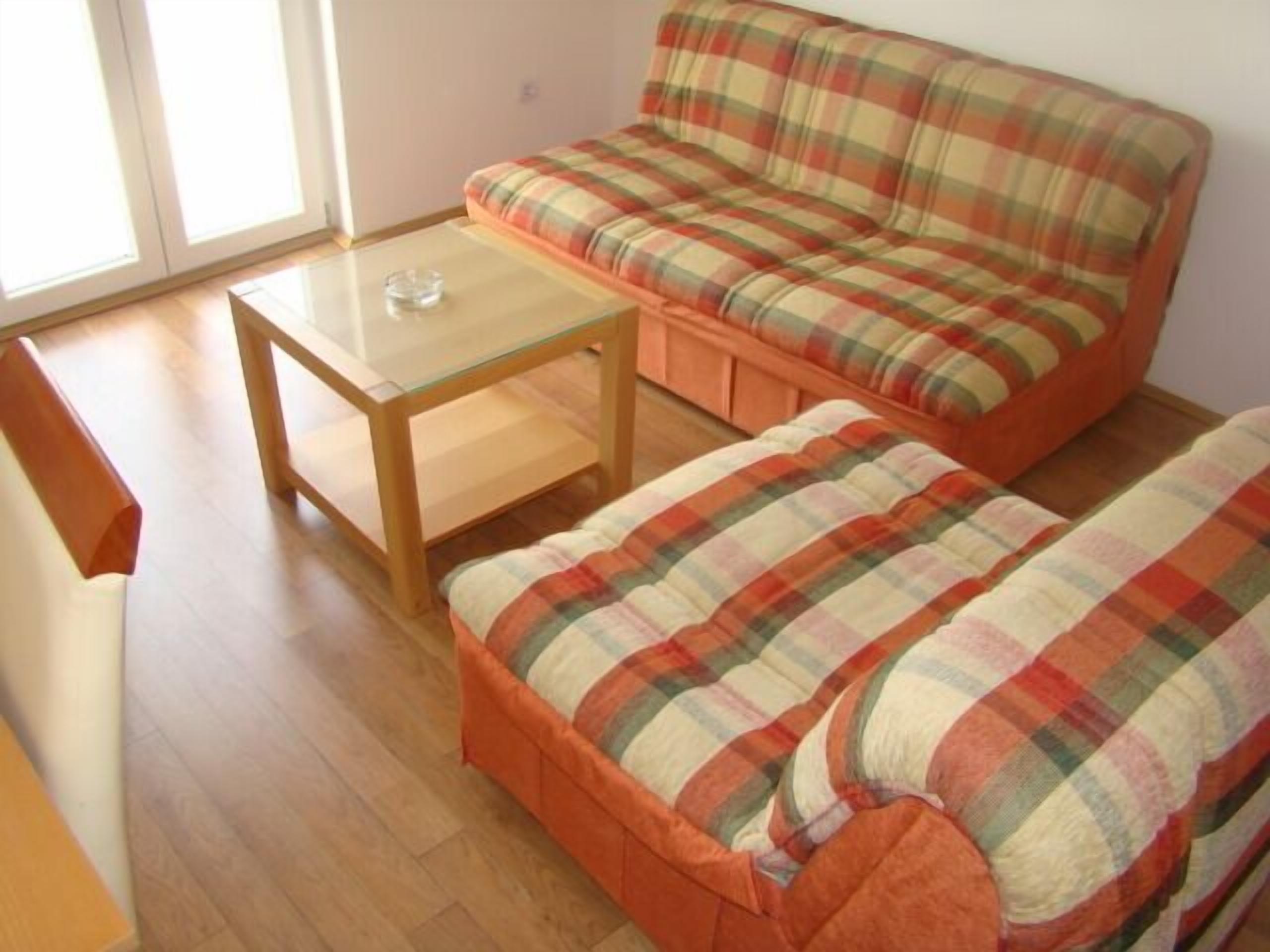 A room with a wooden floor, a plaid sofa, a small table, and a bench.