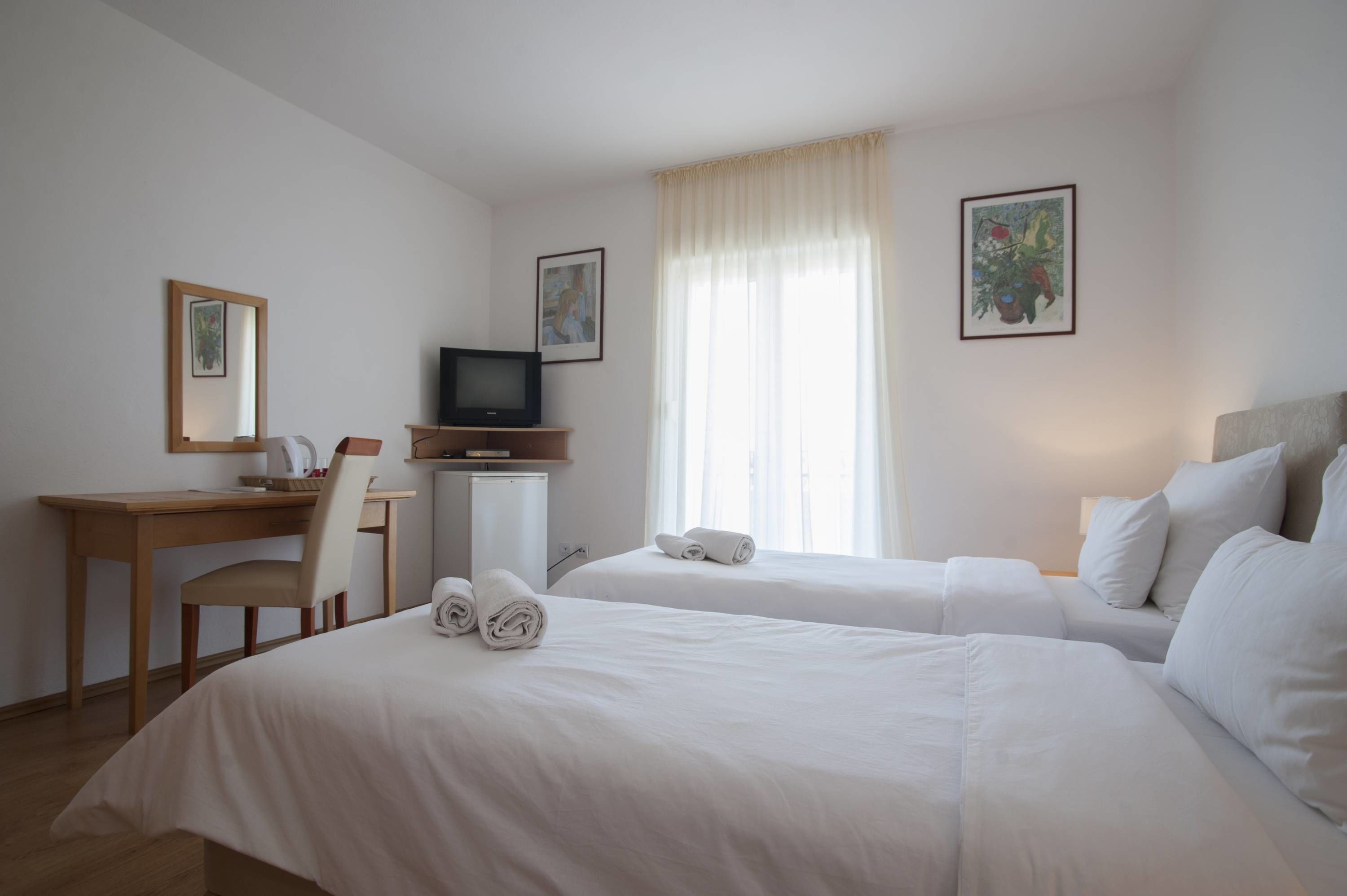 A hotel room with two beds, a desk, a television, and a window with curtains.