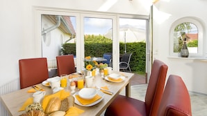 A breakfast table set with croissants, bread, eggs, and juice, with a view of a garden and a building in the background. - Ferienhotel Bernstein (Trassenheide)