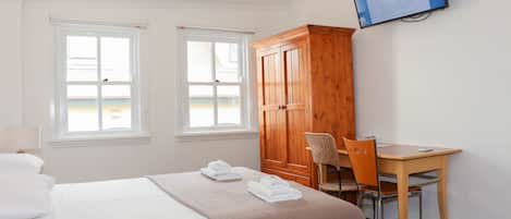 Ett hotellrum med en säng, två fönster, en garderob i trä, ett skrivbord med en stol och en TV som är monterad på väggen.