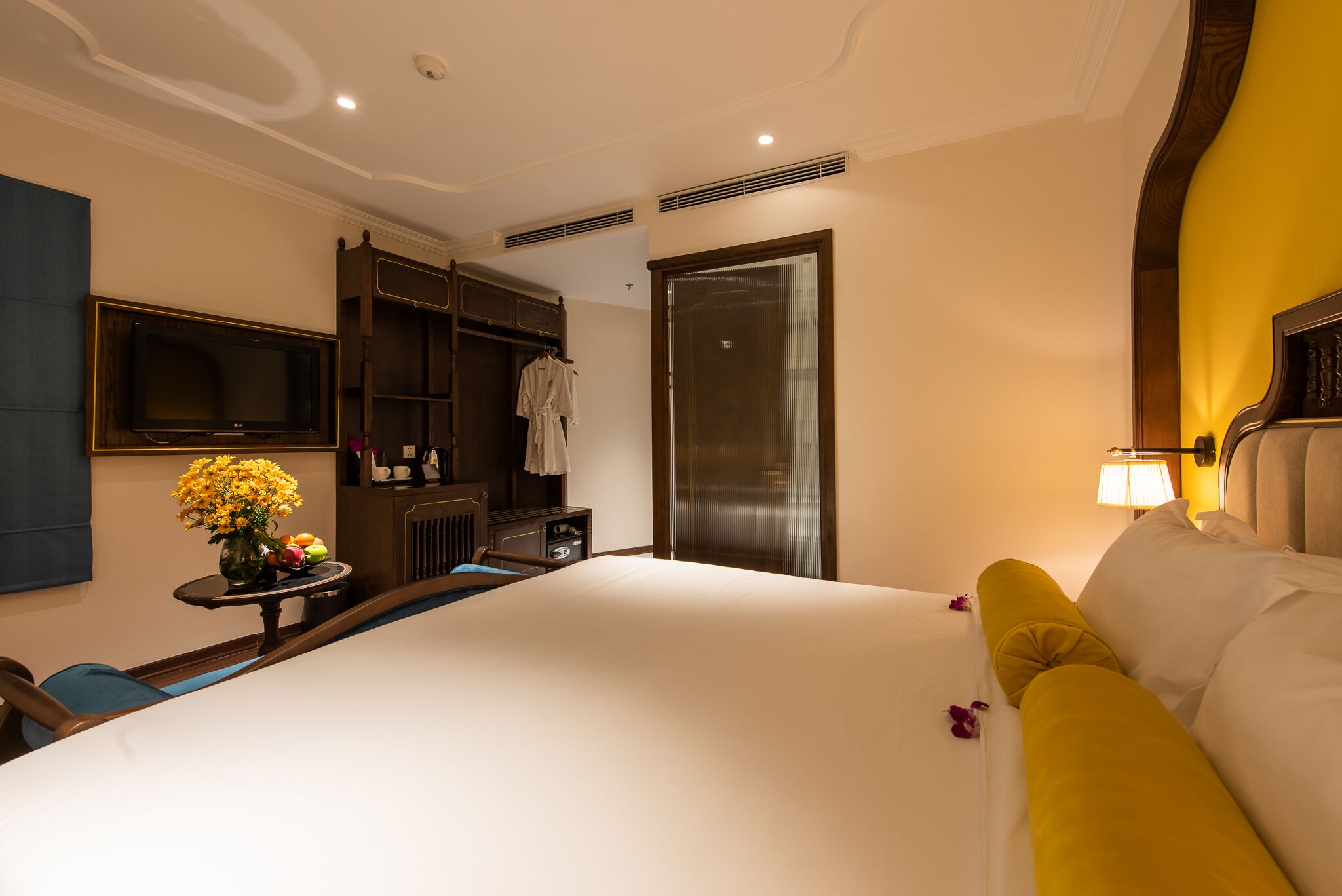 Une chambre d’hôtel avec un grand lit, une armoire, une coiffeuse avec un miroir et un téléviseur fixé au mur.