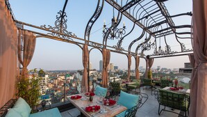 Un área de comedor al aire libre con mesas y sillas, vistas a la ciudad y detalles ornamentales en metal.