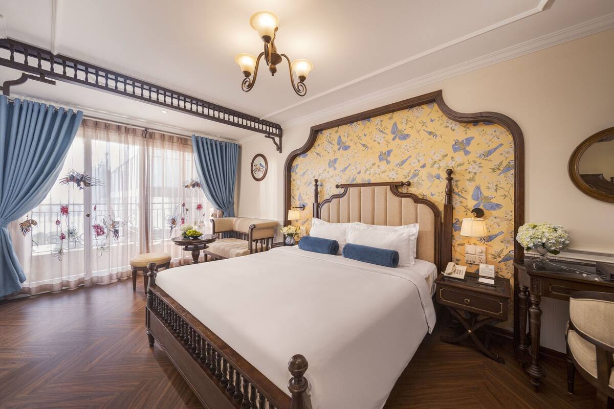 Habitación de hotel con una cama grande, un escritorio con teléfono, una silla y un espejo en la pared.