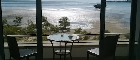 A balcony with a table and two chairs overlooking a beach and the sea.