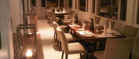 A dining area with tables set for multiple guests, chairs arranged around them, and a lit candle on a table.