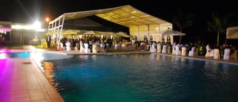 A large outdoor pool area with a covered seating area and a crowd of people.
