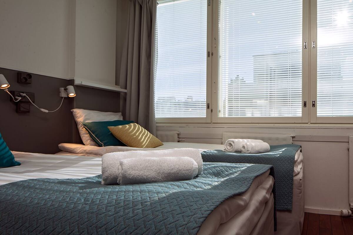 A hotel room with two beds, a chair, and a window with blinds.