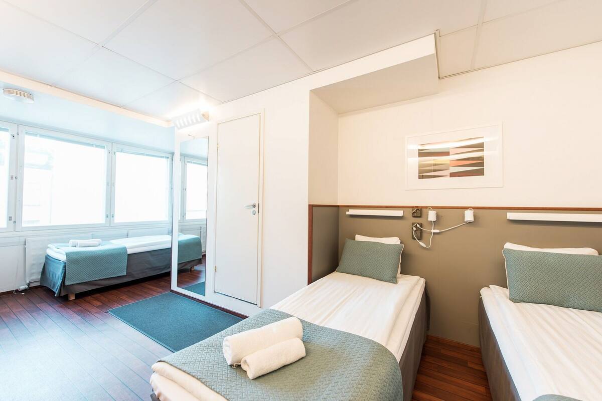 A hotel room with two single beds, a large window, a door leading to a balcony, and a wall-mounted artwork.