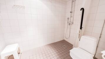 A small, clean bathroom with white tiles, a toilet, a shower, and a handrail.