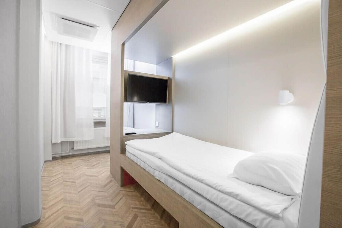 Une chambre d’hôtel moderne équipée d’un lit, d’un téléviseur fixé au mur et d’une lampe de chevet.